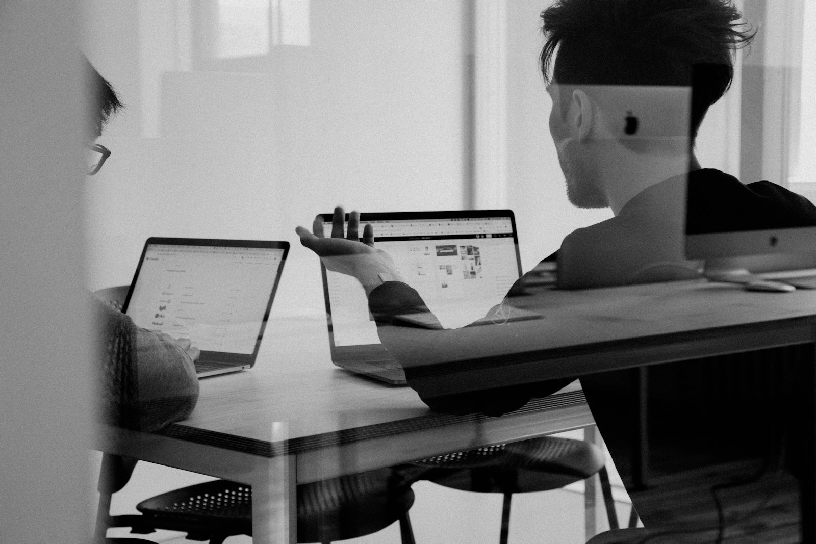 Two colleagues talking through work on their laptops